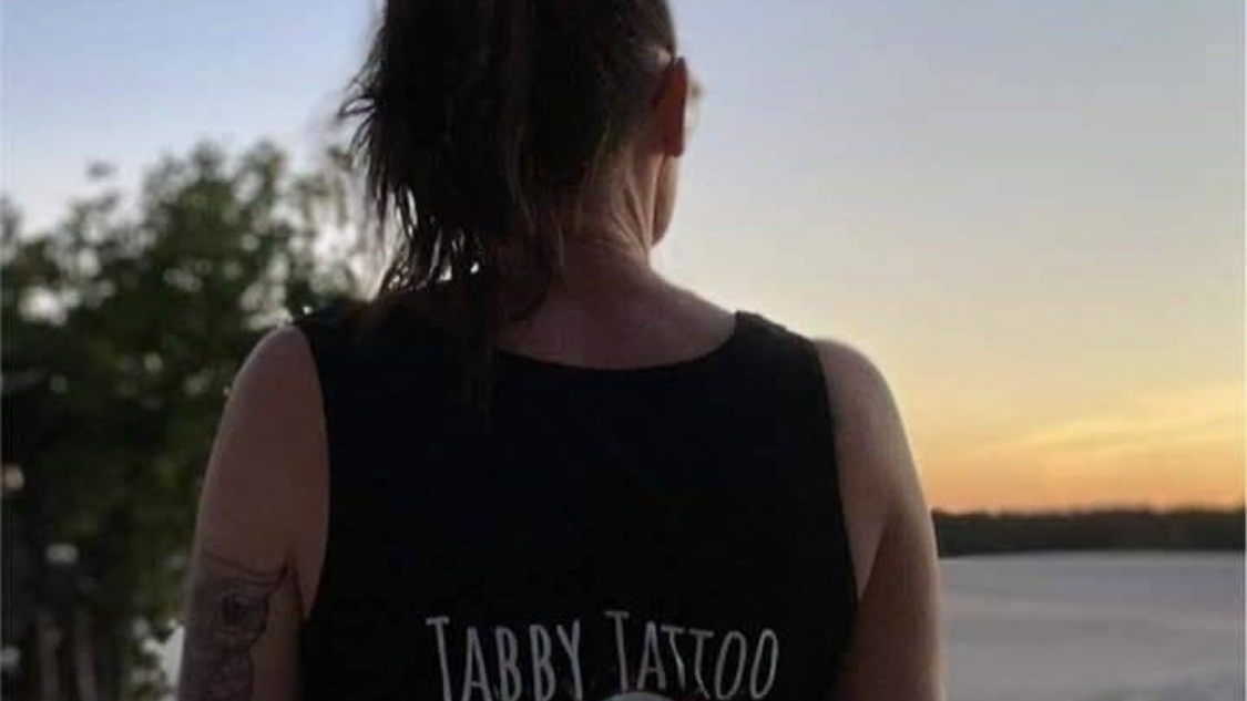 Iemand van achteren bij zonsondergang, met de letters Tabby Tattoo op het zwarte shirt
