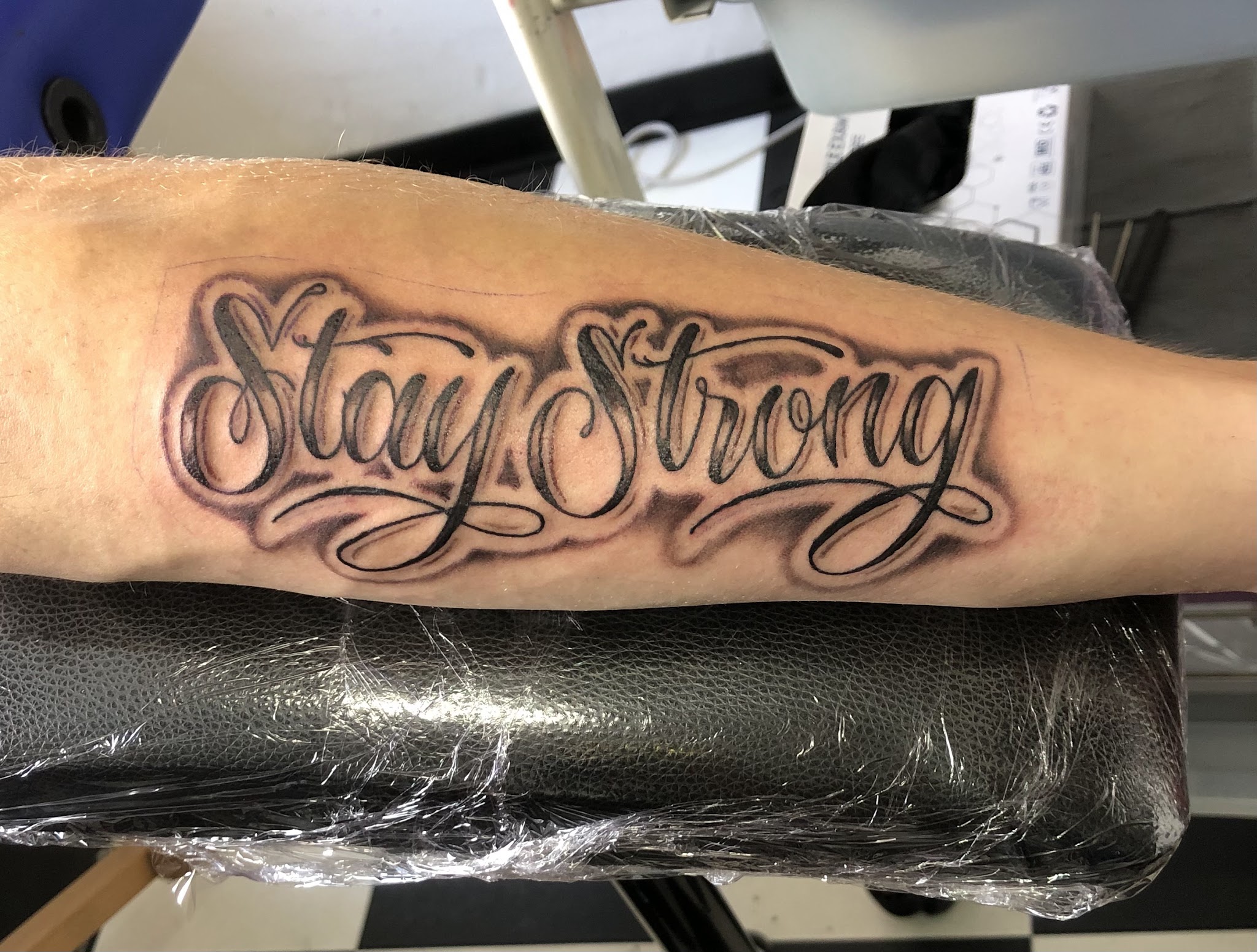 Zwart-grijze letters Stay Strong in sierlijk schrift op een onderarm