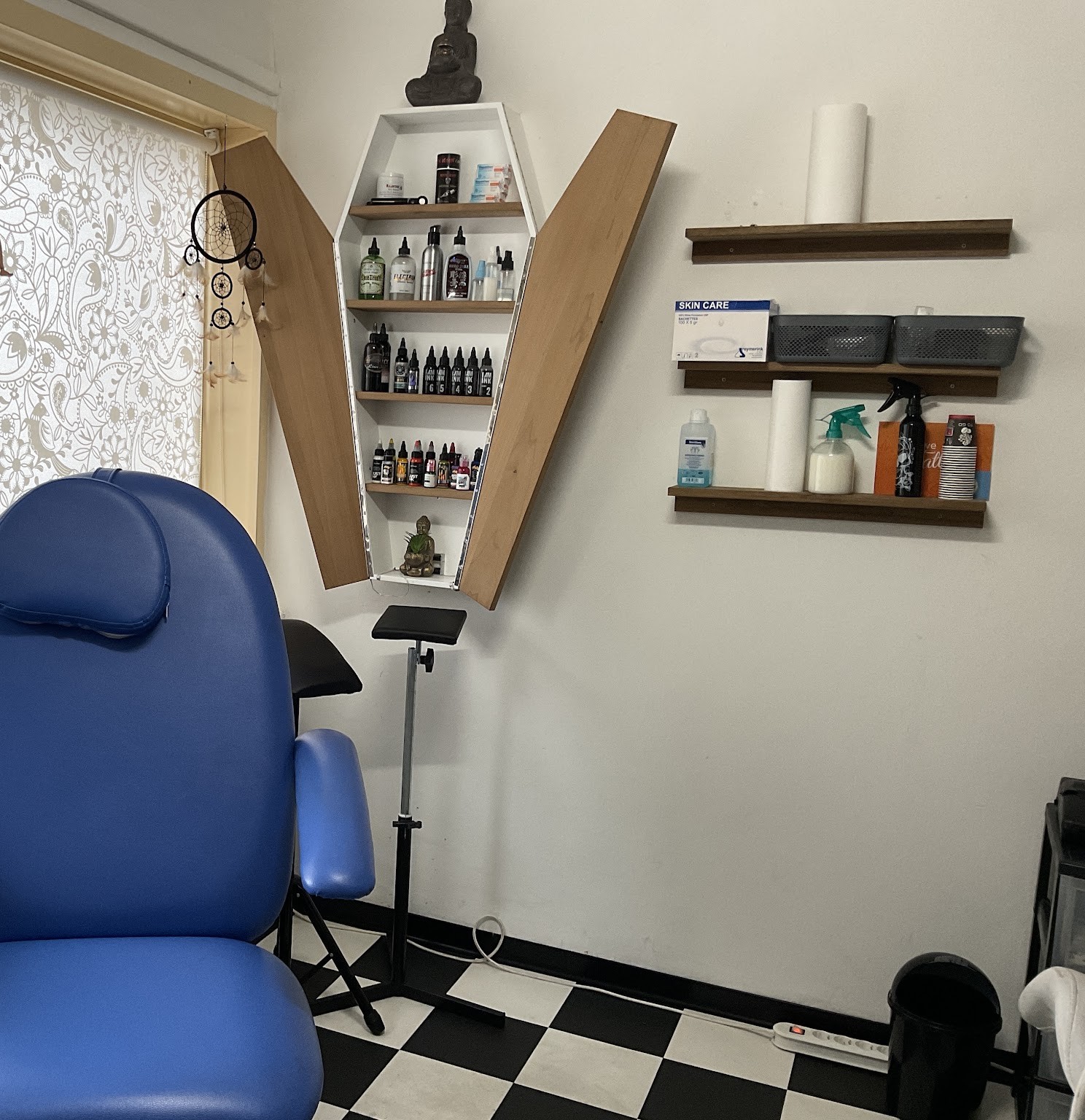 De studio: een blauwe tattoostoel, wandplanken met inkt en een zwart-wit geblokte vloer