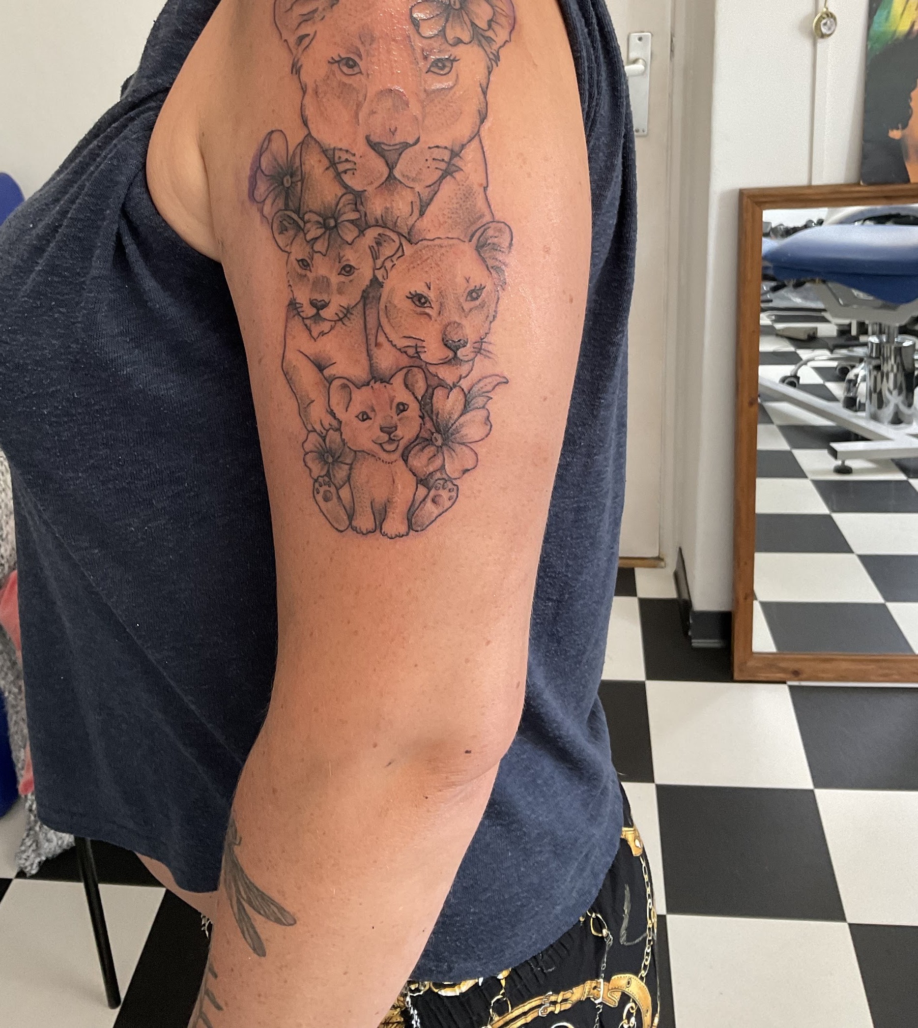 Tattoo van een leeuwin met twee welpjes en bloemen op de bovenarm